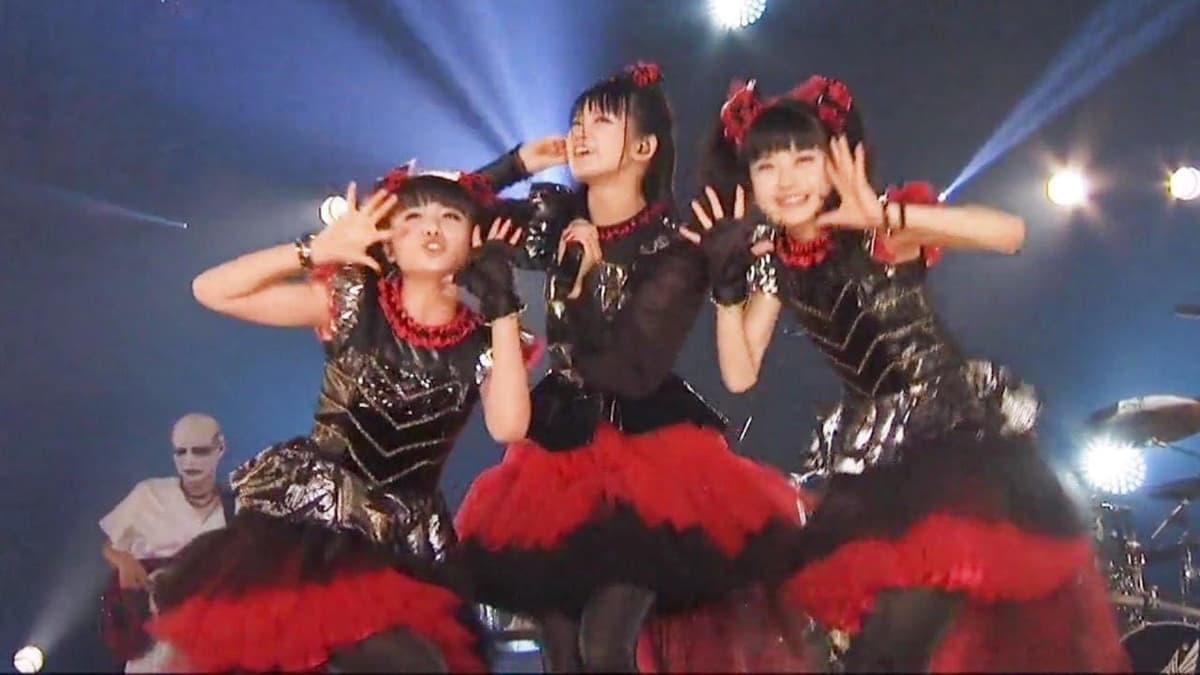 BABYMETAL en el videoclip de Gimme Chocolate!!, las tres integrantes frente a una pantalla gigante con chocolates, el video viral que las lanzó globalmente en 2014